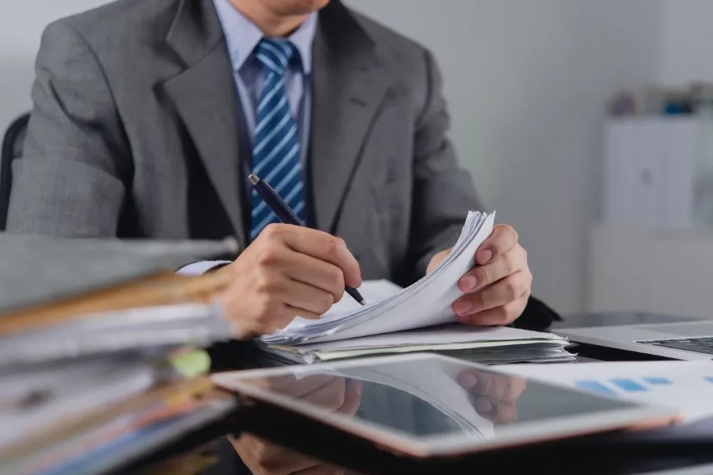 Dirigeant de TPE signant des documents de conformité, entouré de dossiers et de données financières
